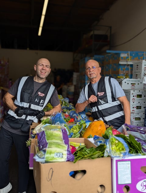 Two workers in safety vests sorting fresh vegetables at a food distribution center
