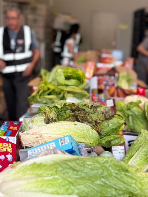 Fresh heads of lettuce and produce displayed on a table with people in safety vests in the background