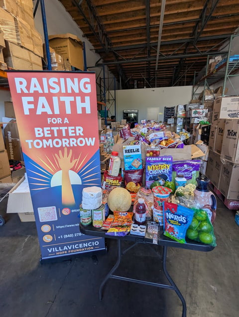 Warehouse display with Raising Faith for a Better Tomorrow sign next to donated food items and supplies for community charity